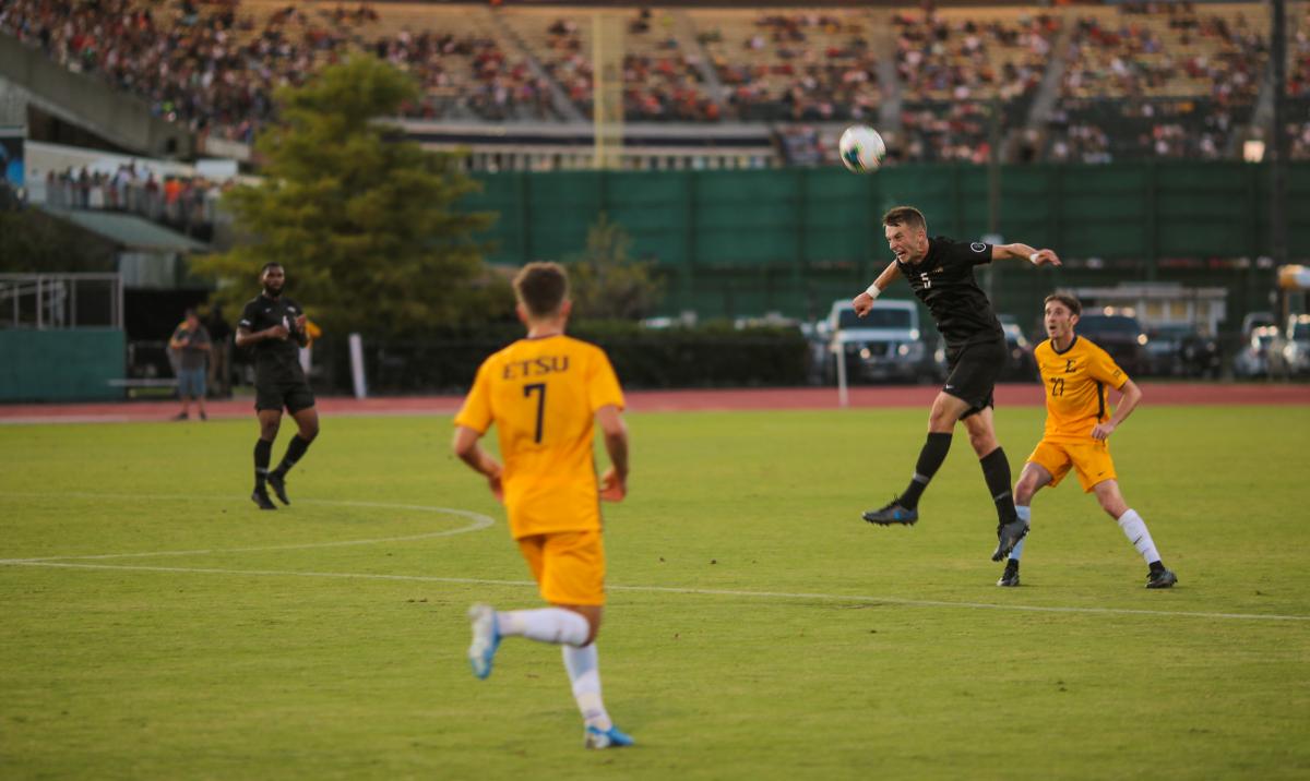 Junior midfielder Simon Fitch heads the ball away from an ETSU player Aug. 30. Photo by Jon Mirador